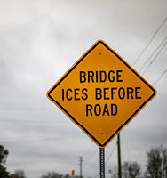 A yellow road sign reads “Bridge Ices Before Road.